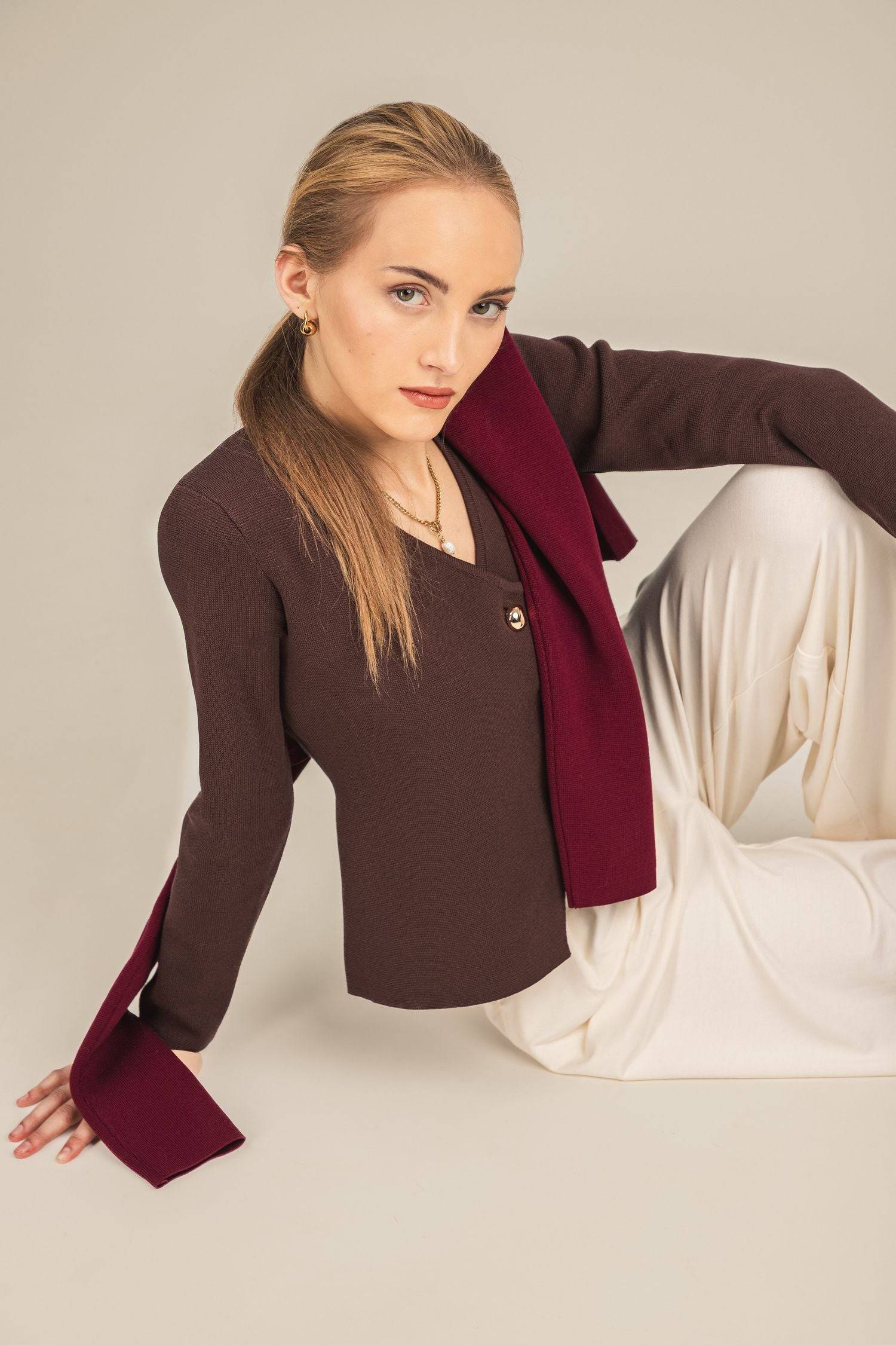 Sweter Amara – elegancki kardigan damski w kolorze brązowym wystylizowany z białymi spodniami i zarzuconym na ramiona bordowym swetrem Amara