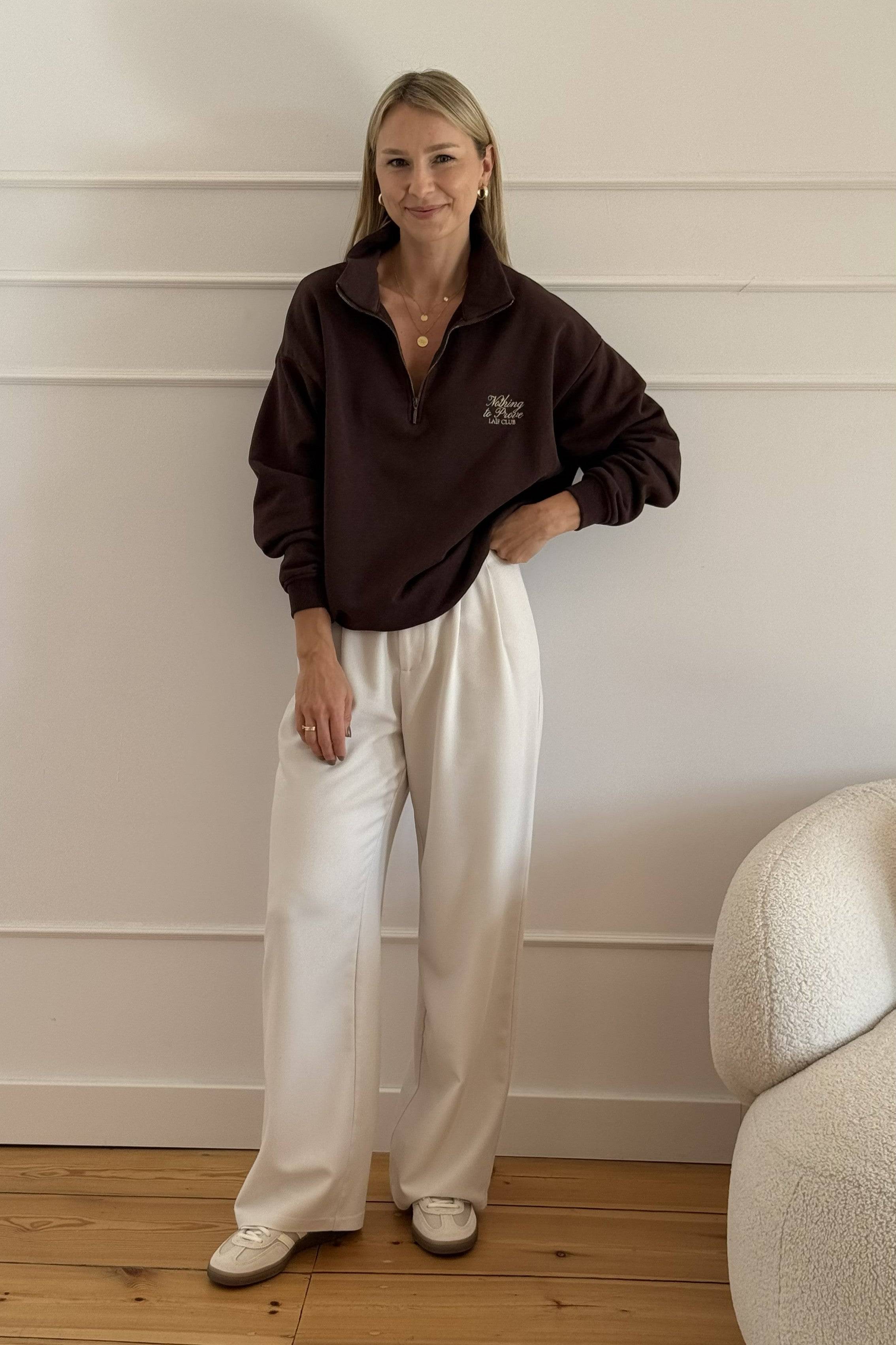 Elegancka bluza damska rozpinana z kołnierzykiem polo w kolorze brązowym z rozpiętym zamkiem. Wystylizowana z białymi, eleganckimi, lejącymi spodniami i złotymi dodatkami w biżuterii