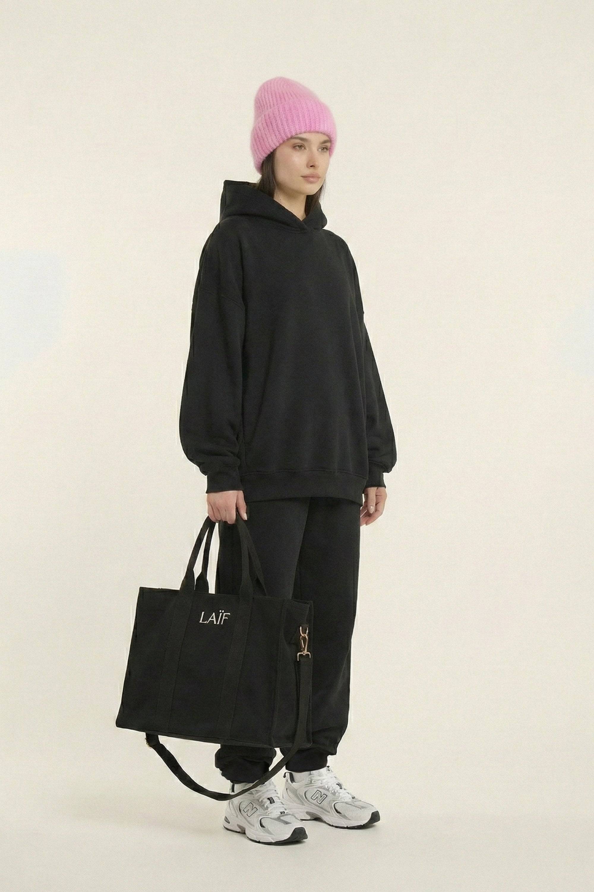 Czarna bluza z kapturem premium z czarnymi dresami, różową czapką i czarną torbą - widok z boku